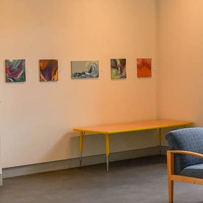 Small, brightly colored paintings line the wall of the Alumni/ae Room