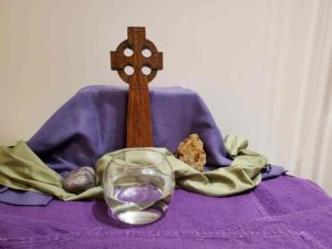 A cross and a bowl of water rest on an altar covered in purple cloth