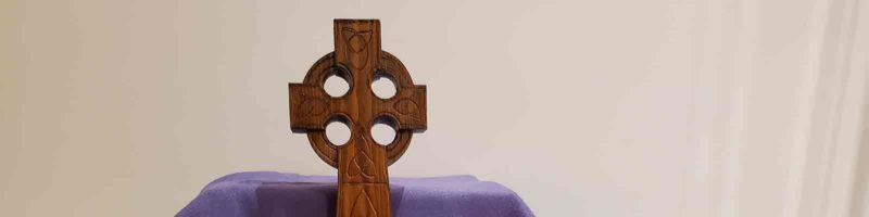 A wooden cross stands resting on a purple cloth.