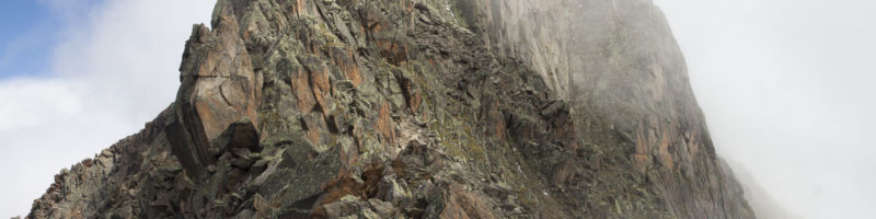 A barren, brown mountain peak is partially hidden by wispy fog.