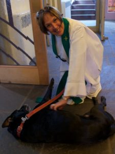 Pastor Kathleen Reed smiles as she kneels on the floor to pet her dog, who is relaxing in the church foyer..