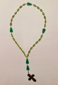 A small cross hangs from a circle of green beads, five large and 28 small.
